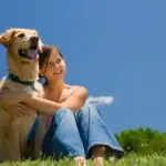 Woman sitting in grass with a golden retriever, blue sky